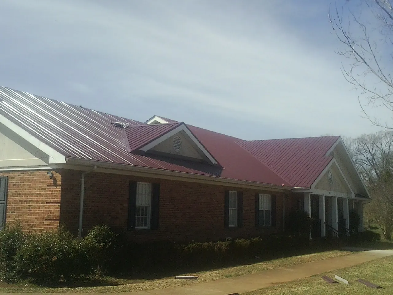 Red metal roof with gabled entries on a long brick building, from a Hail Damage Roof Repair job in Vermilion