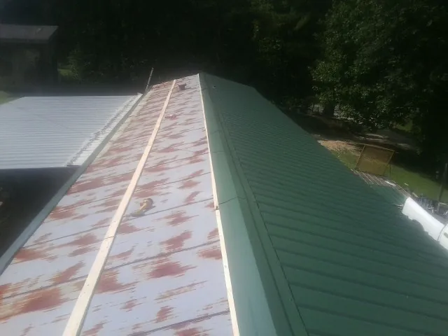 Old rusted panels beside newly installed green metal roofing — Wind Damage Roof Repair by Roofing Brothers in Vermilion