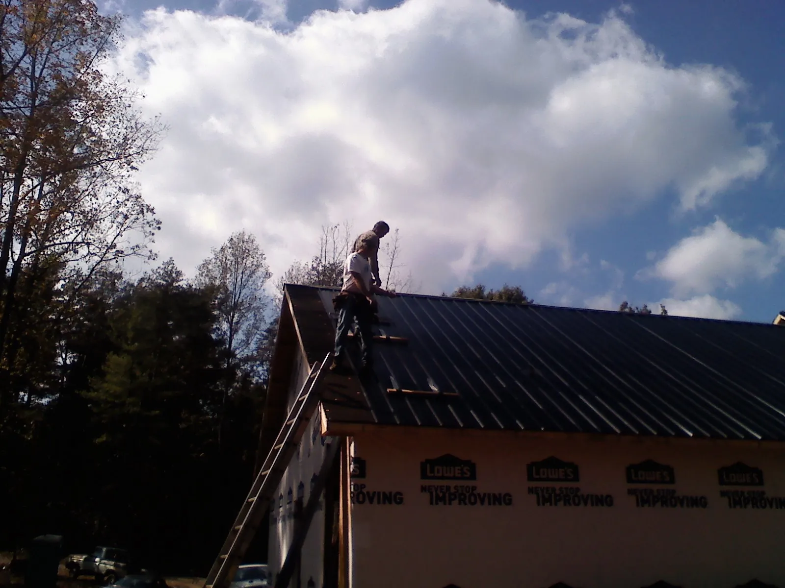 Roofer fastening dark metal panels high against a cloudy sky, from a Roof Inspection job in Vermilion