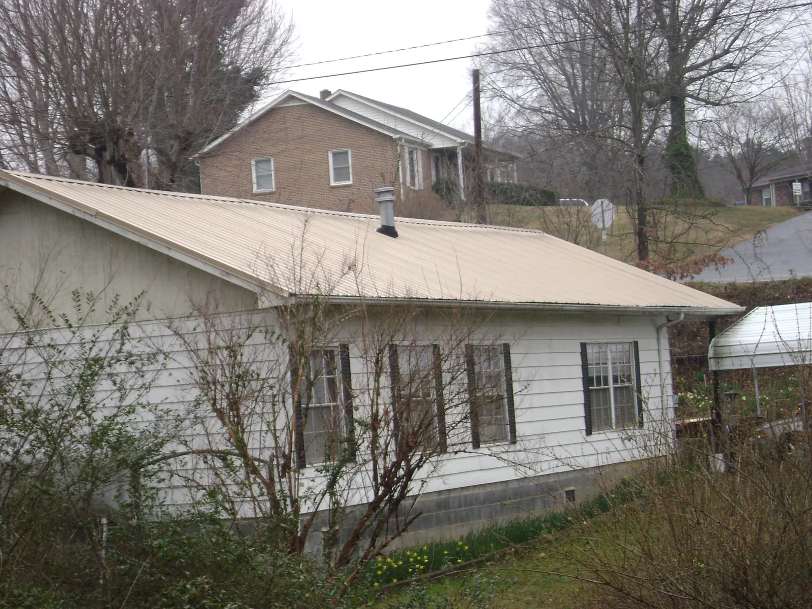 Tan metal roof on a white sided house set into a hillside — Commercial Roofing by Roofing Brothers in Vermilion