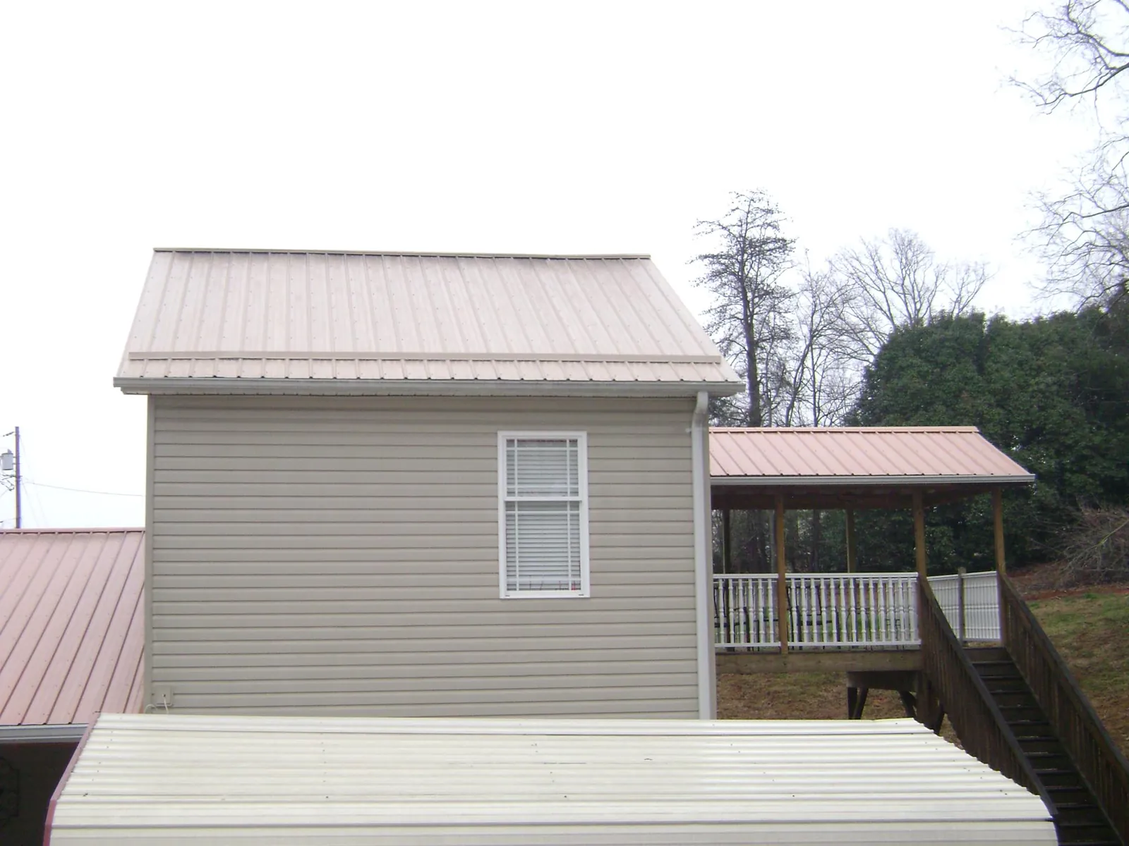 Tan metal roofs on a two story addition and attached porch, from a Roof Replacement job in Vermilion